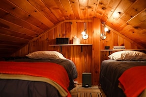 Ein gemütliches Schlafzimmer im Dachgeschoss mit zwei Betten, Holzwänden und einem kleinen Bücherregal.