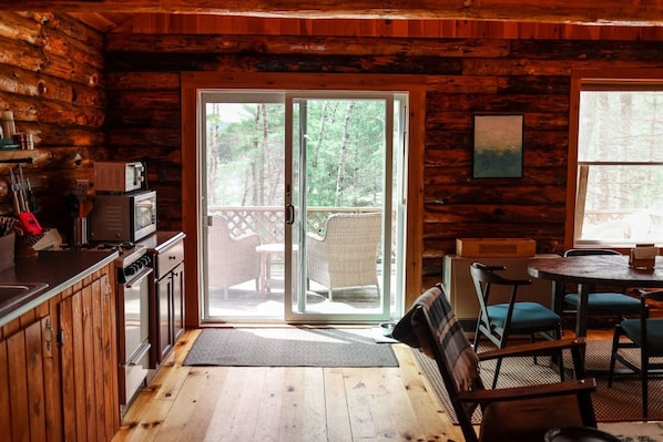 A cabin interior with a kitchen, dining area, and a sliding glass door leading to an outdoor deck. - Long Pond Cabin Retreat (Denmark)