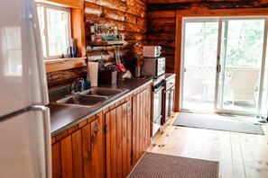 Eine Küchenzeile in einer Holzhütte mit Holzschränken, einem Kühlschrank, einer Mikrowelle und einem Spülbecken.