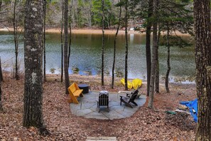 A lakeside campsite with a fire pit, chairs, and a covered area.