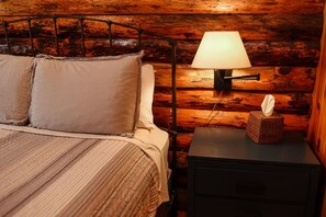 A wooden cabin-style room with a bed, a bedside lamp, and a nightstand with a tissue box.