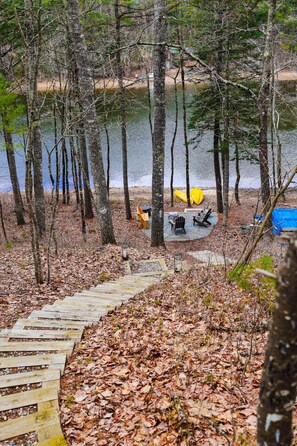 A forested area with a wooden deck leading to a campsite by a lake.