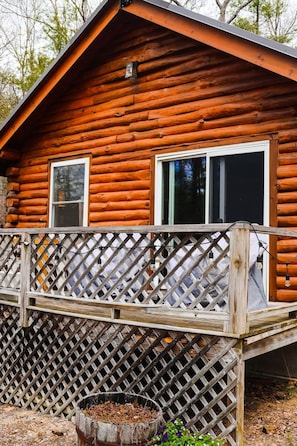 A log cabin with a wooden deck and a lattice railing.