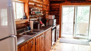 Mökkitunnelmainen keittiö, jossa on puuseinät, jääkaappi, kaksialtainen tiskiallas ja liukuovi, joka johtaa ulkotilaan.