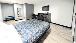 Ein Hotelzimmer mit einem Bett, einem Schreibtisch mit Fernseher, einem Spiegel und einer Sitzbank.