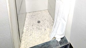 Eine bodenebene Dusche mit Glastür, Marmorwänden und einem Boden aus sechseckigen Fliesen.