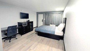 Ein Schlafzimmer mit einem Bett, einem Schreibtisch, einem Stuhl, einem Fernseher und einer Tür.