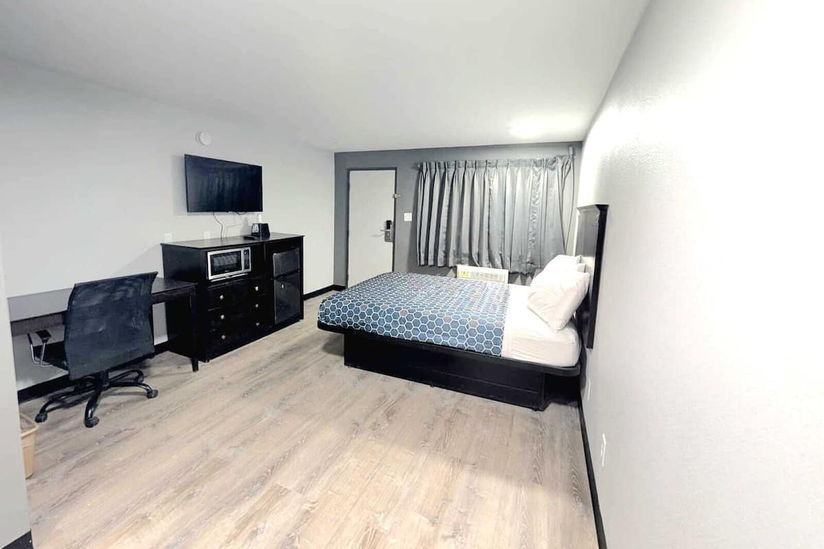 A bedroom with a bed, a desk, a chair, a television, and a door.