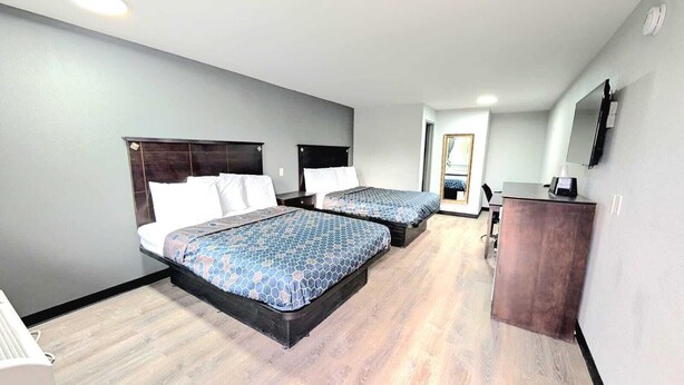 Ein Hotelzimmer mit zwei Betten, einem Schreibtisch, einem Spiegel und einem Fernseher.