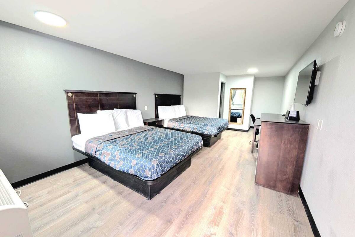 A hotel room with two beds, a desk, a mirror, and a television.
