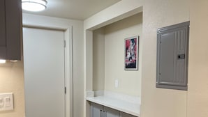 Cozinha com bancada branca, armários cinzentos, uma porta e luminária fixada na parede.