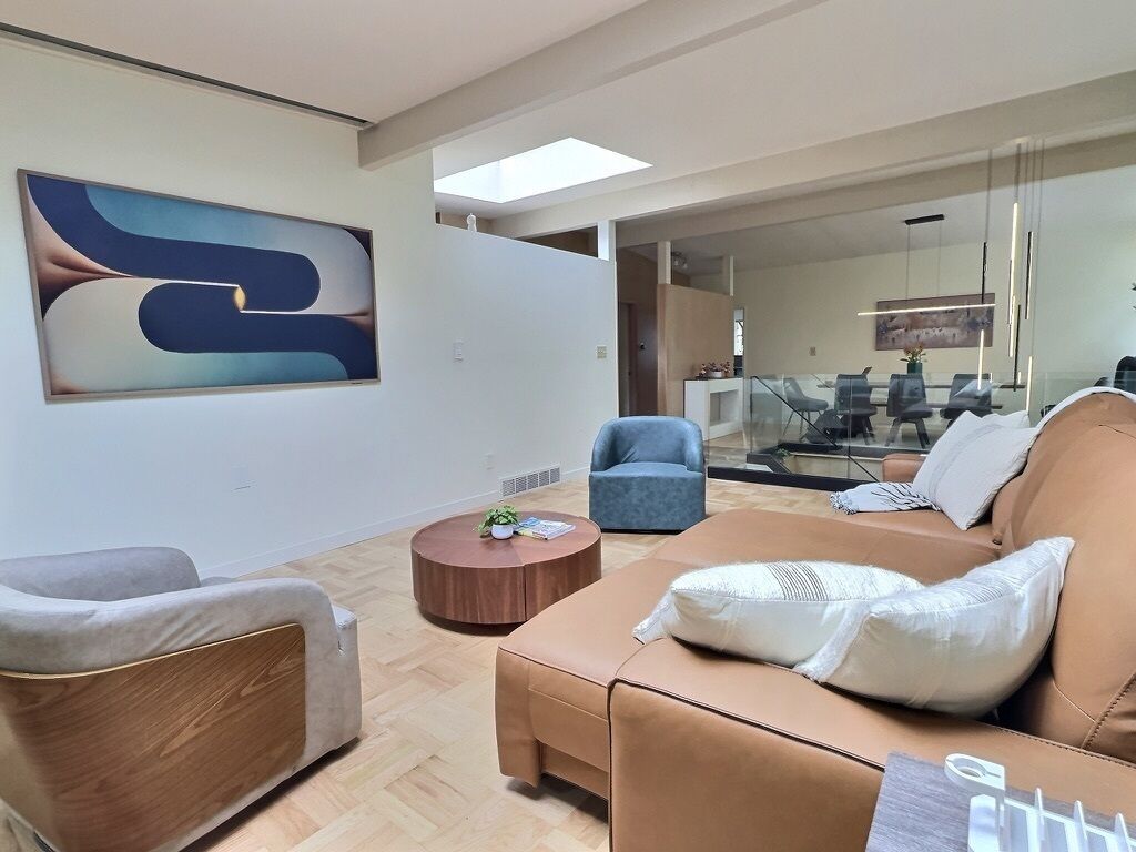 A modern interior with a large abstract painting, a brown leather sofa, a round wooden coffee table, and a blue armchair.