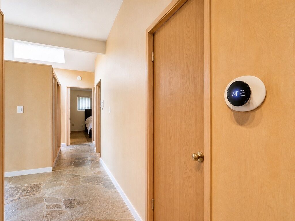 Un couloir doté d’un sol en pierre, de portes en bois et d’un thermostat fixé sur l’une des portes.