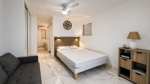 A bedroom with a bed, a sofa, a wooden cabinet, a ceiling fan, and a wall clock. - Le Cocon Bleu - 2 steps from the beach 🌴✨ (Le Moule)