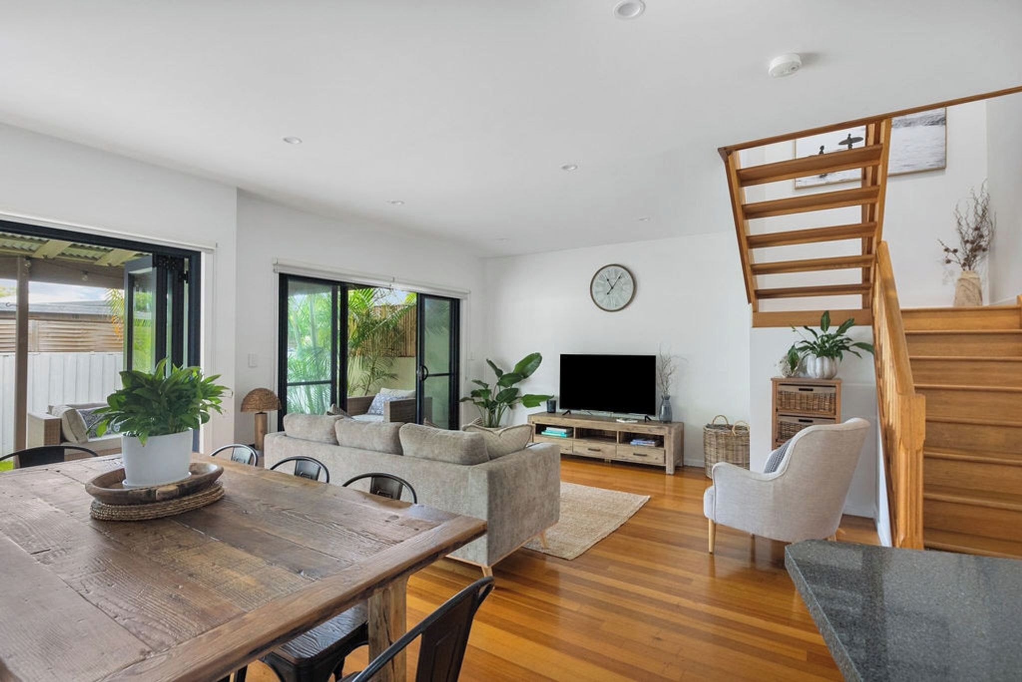 Un salon moderne avec une table à manger en bois, un canapé, un téléviseur et un escalier.
