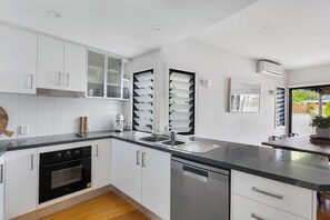 Una cocina moderna con armarios blancos, horno empotrado, lavavajillas y un ventanal grande.
