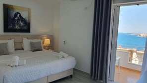 A hotel room with a bed, a nightstand, a lamp, a painting on the wall, and a balcony with a view of the sea. - Hotel Ceko (Sarandë)