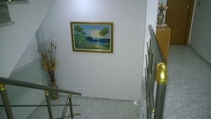 A staircase with a railing, a painting of a beach scene, and a vase with flowers on the wall. - Hotel Ceko (Sarandë)