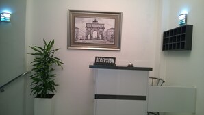 En receptionsdisk med en skylt som visar ordet ”RECEPTION”, en inramad bild av en historisk byggnad och en krukväxt.