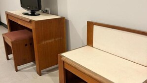 A wooden desk with a television, a small bench, and a wall-mounted shelf.