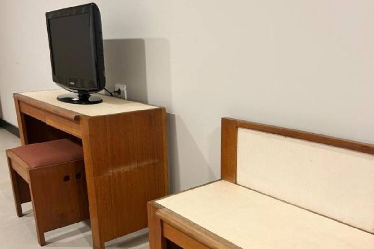 A wooden desk with a television, a small bench, and a wall-mounted shelf.
