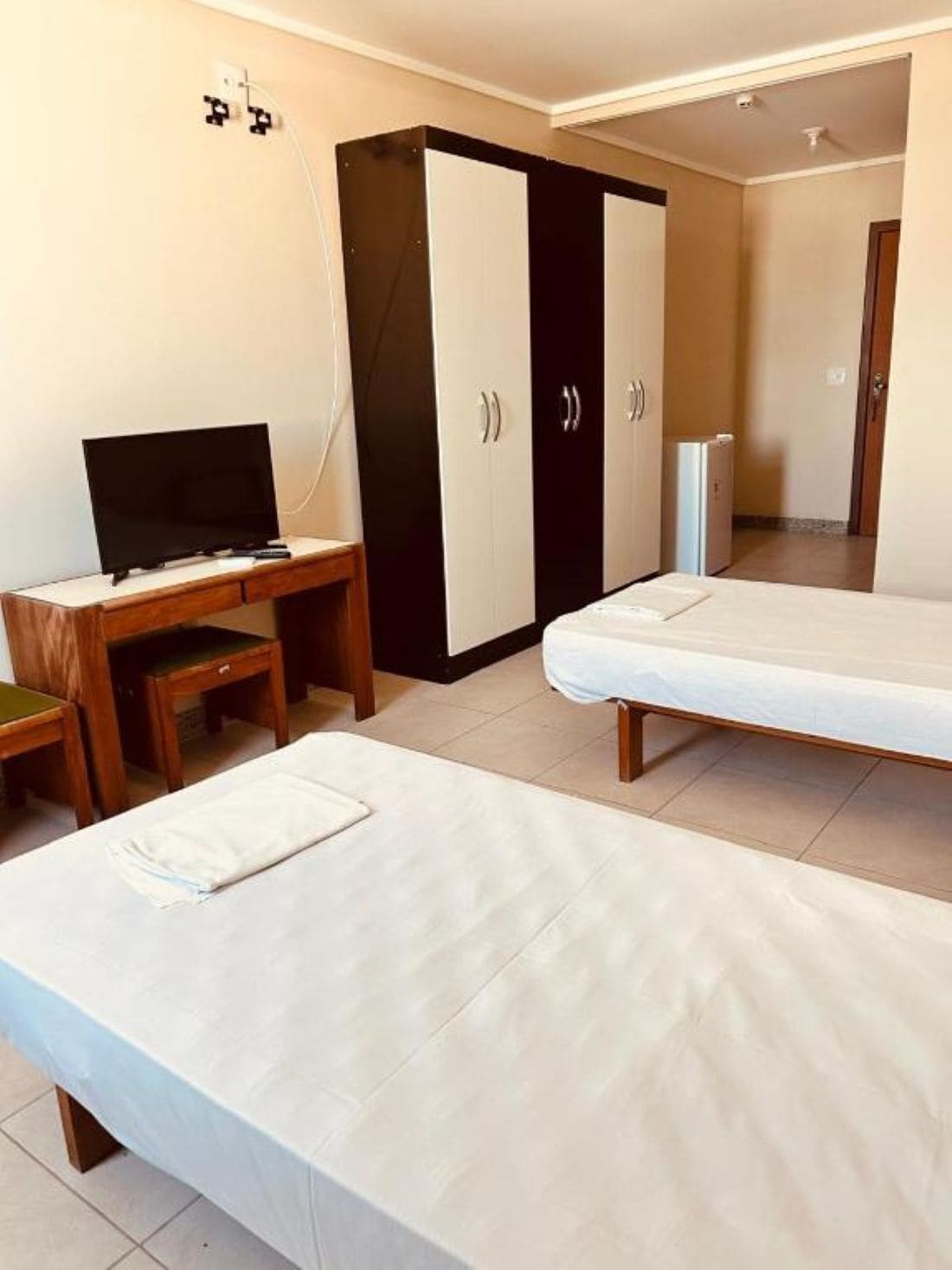 A hotel room with a bed, a desk with a TV, a wardrobe, and a refrigerator.