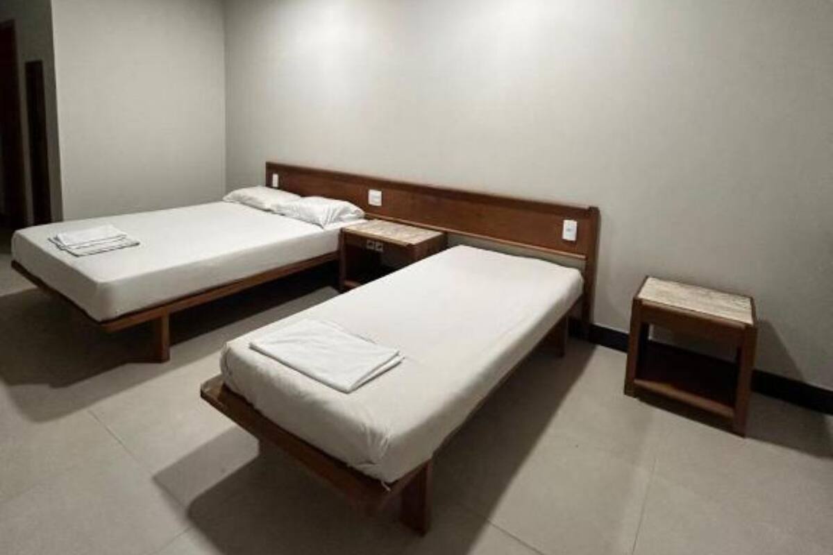A room with three single beds, wooden headboards, and a small wooden nightstand.