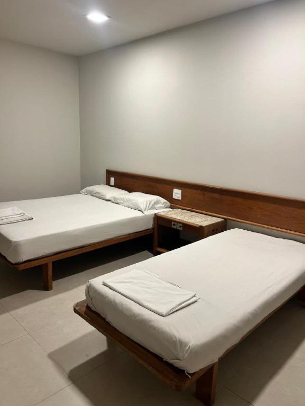 Quarto de hotel com duas camas de solteiro, cabeceira de madeira, mesa de cabeceira e pequena mesinha de apoio.