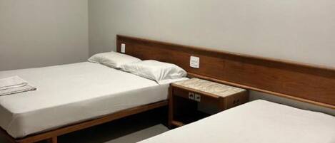 Habitación de hotel con dos camas individuales, un cabecero de madera, una mesita de noche y una pequeña mesita auxiliar.