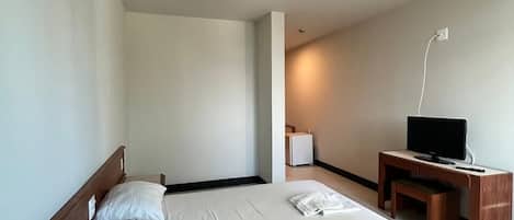 Una habitación de hotel con cama, escritorio, televisor y lámpara.
