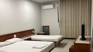 A hotel room with two beds, a desk, a chair, an air conditioning unit, and a television.