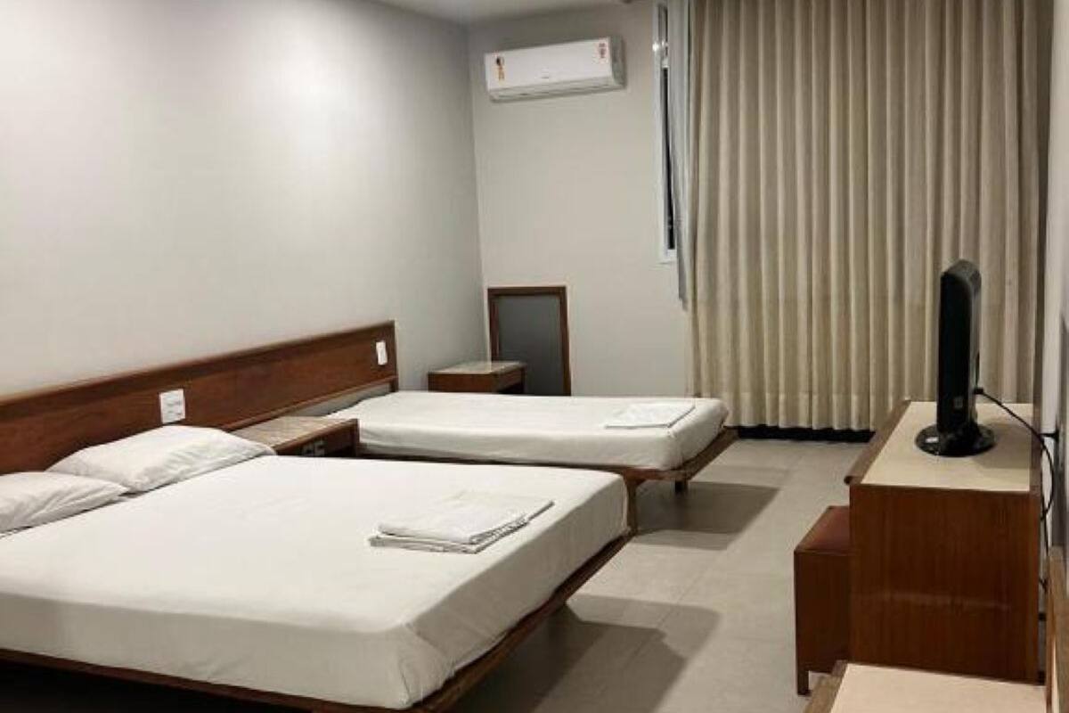A hotel room with two beds, a desk, a chair, an air conditioning unit, and a television.