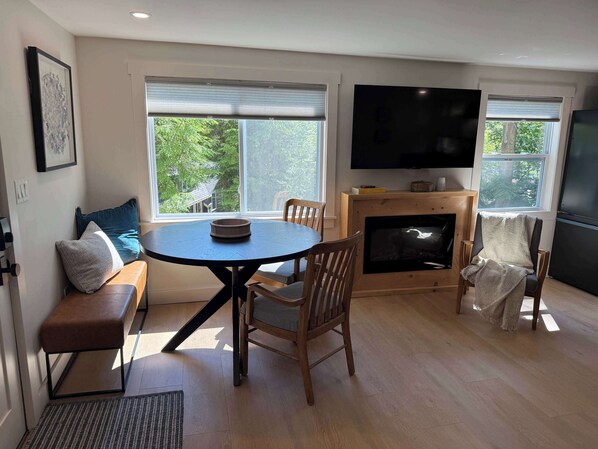 A modern living room with a round table, wooden chairs, a sofa, a fireplace, and a large TV.