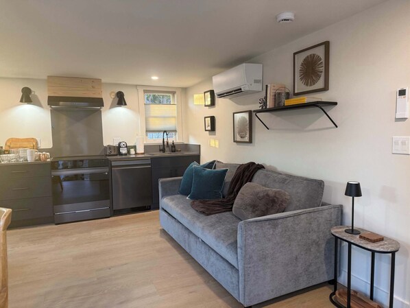A compact living space with a kitchenette, grey sofa, and a small side table.
