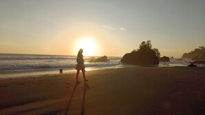 Scena di spiaggia con una persona che cammina, onde dell'oceano e un tramonto.