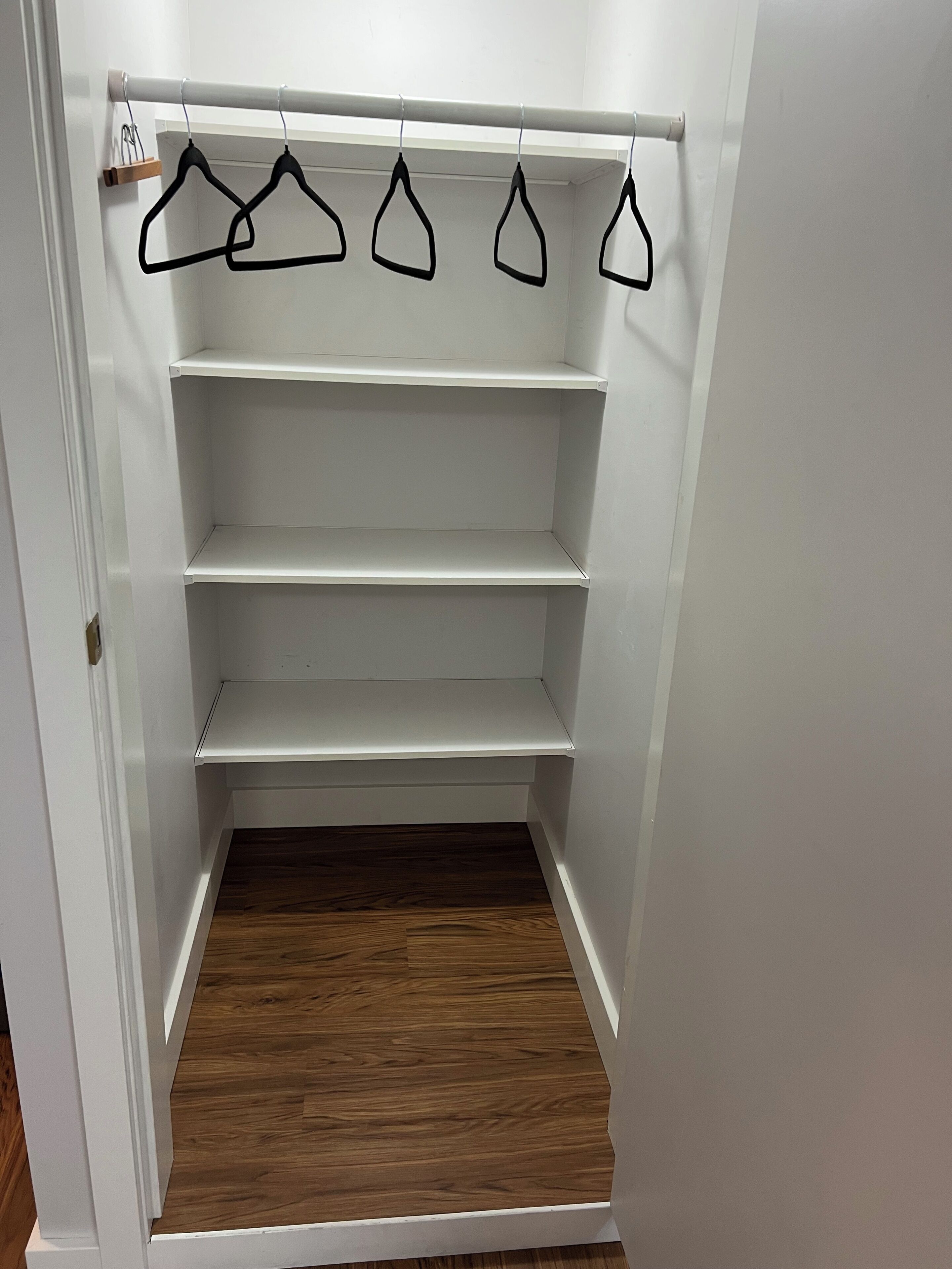 A closet with four shelves and four black hangers on a rod.