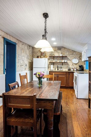 A rustic kitchen with wooden cabinets, a white refrigerator, and a hanging light fixture. - Hoerster Historic 1800s Sunday Haus, Close to Main (Fredericksburg)