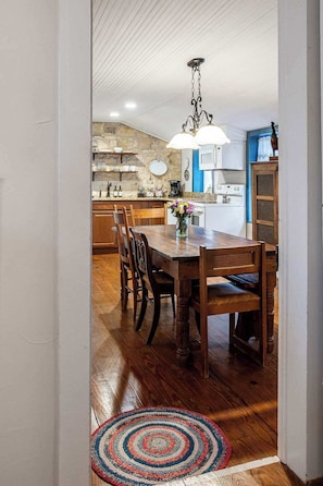 A kitchen with a stone backsplash, wooden cabinets, a dining area with a wooden table and chairs, and a hanging light fixture. - Hoerster Historic 1800s Sunday Haus, Close to Main (Fredericksburg)