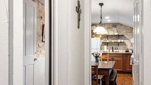 Ein Flur, der zu einer Küche mit Steinwand, Holzboden und einem Essbereich mit Stühlen und Tisch führt.