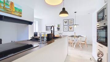 A modern kitchen with a central island, pendant lighting, and a dining area with chairs.