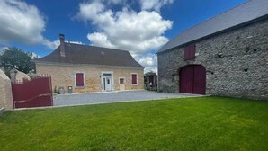 A stone building with a red door and windows, a paved driveway, and a grassy area in front. - La petite Maison Rouge, Charm and Nature in Béarn (Igon)