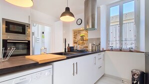 A modern kitchen with white cabinetry, a built-in oven, a stainless steel range hood, and a wooden countertop. - La petite Maison Rouge, Charm and Nature in Béarn (Igon)