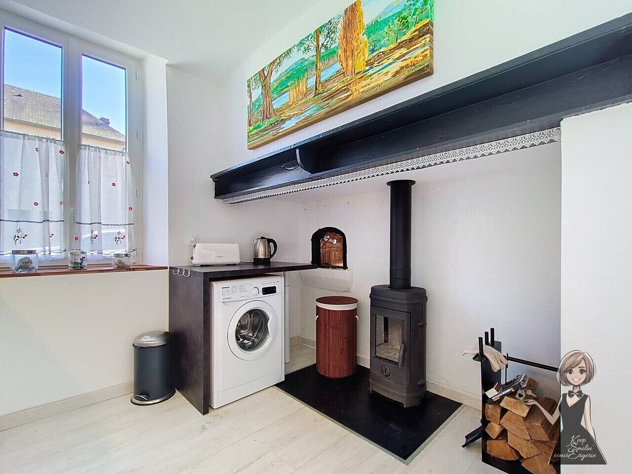 A compact kitchen with a washing machine, a wood-burning stove, and a window with curtains.