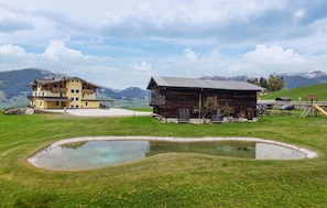Ein Berggrundstück mit Teich, einer Holzhütte und einem gelben Gebäude mit Balkonen.