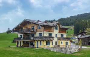 A large two-story house with multiple balconies, a stone foundation, and a hillside backdrop. - Awesome apartment in Hollersbach (Hollersbach)