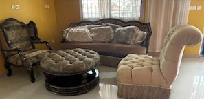 Ein Zimmer mit einer Couch, einem Sessel und einem runden Hocker.