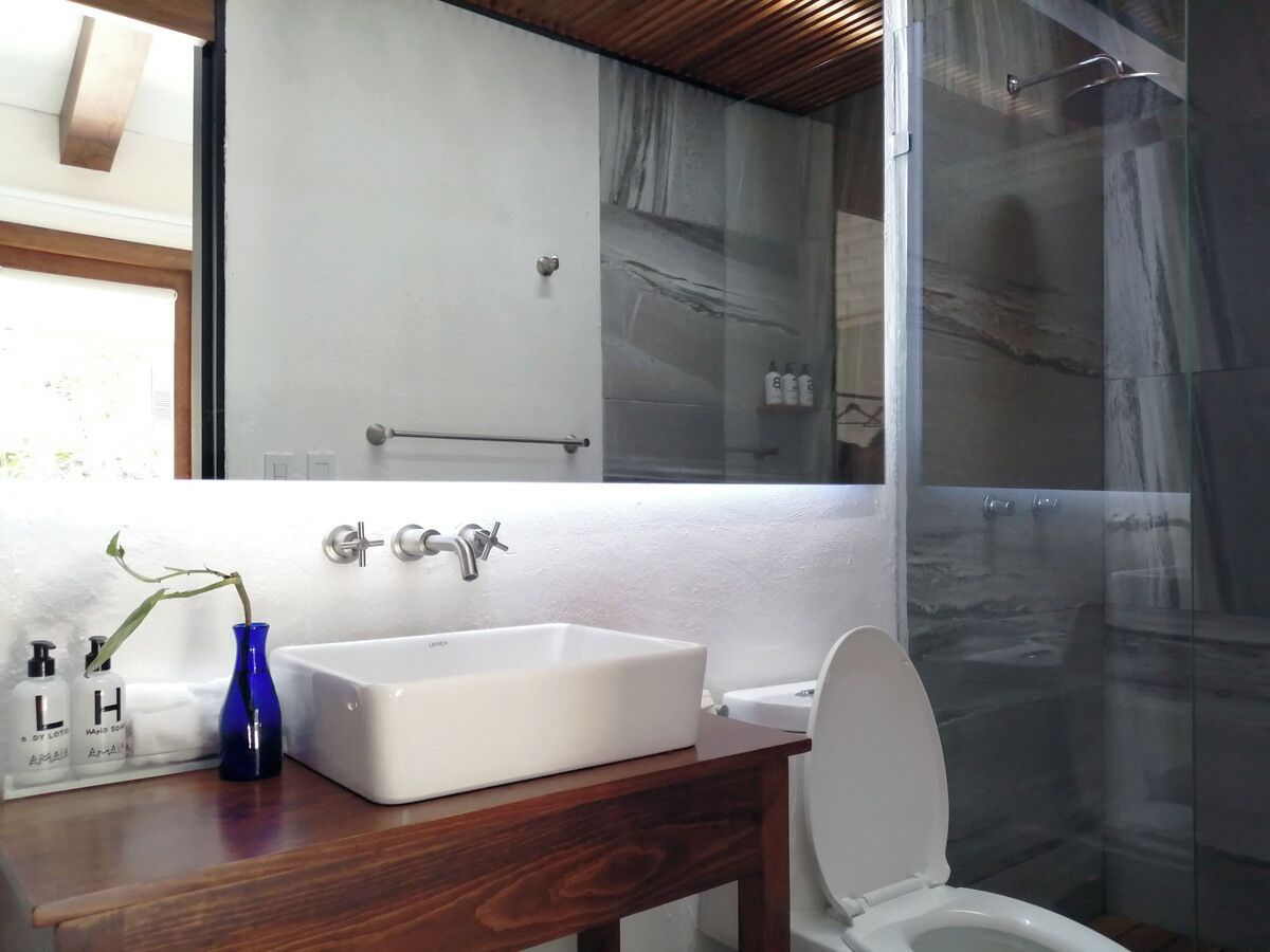 A bathroom with a white sink, a wooden vanity, a blue vase, and a glass shower enclosure.