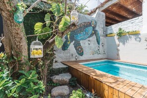 Ein Schwimmbecken mit Holzterrasse, Wandgemälde einer Meeresschildkröte und Vogelkäfig mit Zitronen.