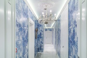 Ein Flur mit blauen Wandmustern, einer Chandelüster und einer Tür am Ende.