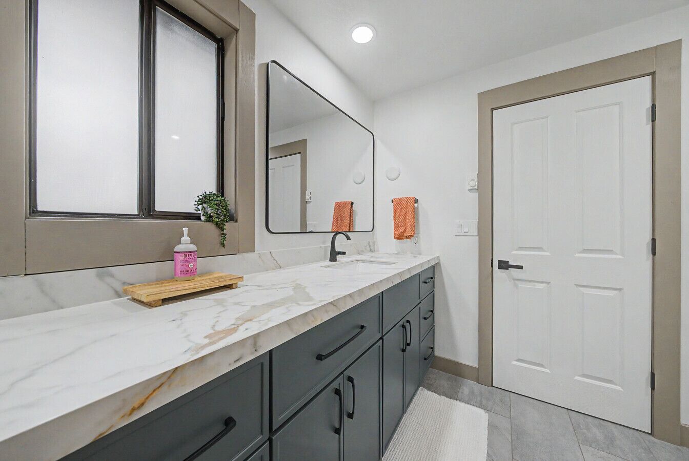 A bathroom with a marble countertop, a mirror, a sink, a towel rack, and a door.